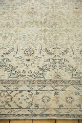 Distressed texture of vintage Oushak rug, showing pale ivory field and earth-tone outlines.