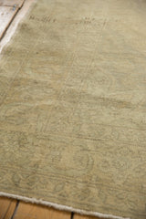 Distressed Oushak carpet pile texture in soft beige and slate green with raw edge.
