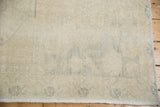 Distressed Oushak rug corner showing blanched pile, faint patterns, and woven edge.