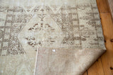 Distressed vintage Oushak rug showing aged brown patterns and folded woven foundation.