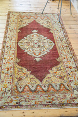 Detail of Oushak rug lower border, cinnabar field, ivory, orange floral motifs, and fringe.