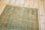 Worn texture of a distressed Belouch runner, showcasing soft green and charcoal patterns.