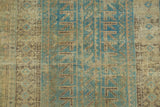 Distressed Belouch rug detail, showcasing geometric blue, soft green, and charcoal brown motifs.