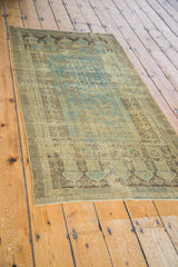 Distressed Belouch rug section: faded soft green, charcoal brown, and blue geometric patterns.