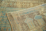 Distressed Belouch rug: geometric aqua, charcoal brown, ivory patterns, and its woven foundation.
