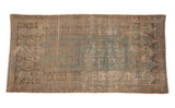 Aged texture, faded green and brown geometric patterns on a distressed Belouch rug corner.