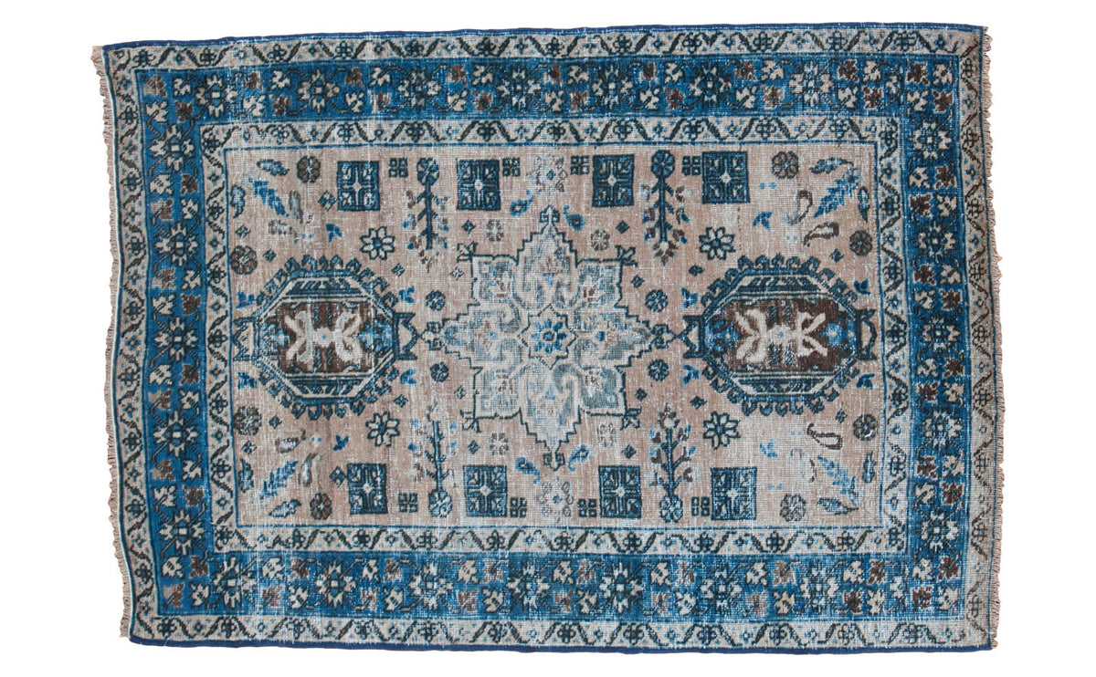 Distressed vintage Heriz rug with neutral antique ivory ground and meandering blue patterns.