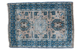 Distressed vintage Heriz rug with neutral antique ivory ground and meandering blue patterns.