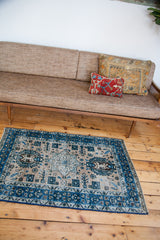 Angled view of distressed vintage Heriz rug, blue geometric border, and ivory field motifs.