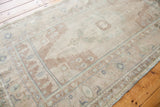 Vintage Oushak rug corner showing sandy beige field and faded blue-green geometric border.
