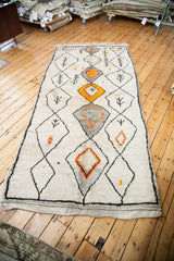 Fringed bottom edge of vintage Moroccan runner, showing shaggy ivory pile and saffron, orange-red diamond.