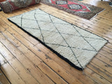 Geometric black lattice diamond motif on the shaggy ivory pile of this Moroccan rug.