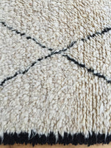 Shaggy ivory wool pile with black lattice motif and thick fringe detail.