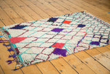 Shaggy ivory pile, vibrant red, purple, blue geometric diamonds, and colorful fringed edge.