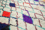 Textured vintage Moroccan rug pile with ivory, red, purple, and blue diamond pattern.
