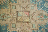 Geometric field detail with central pastel-colored square motif on beige, framed by aqua blue.