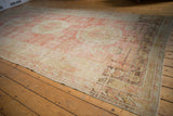Angled view of a distressed antique Khotan carpet highlighting its soft red field and triple medallions.
