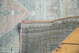 Corner of vintage Oushak rug exposing hand-woven backing and faded peach, grey pattern.