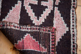 Folded corner of vintage Kars rug, displaying deep background, grapefruit red stepped-geometric triangles, and weave.