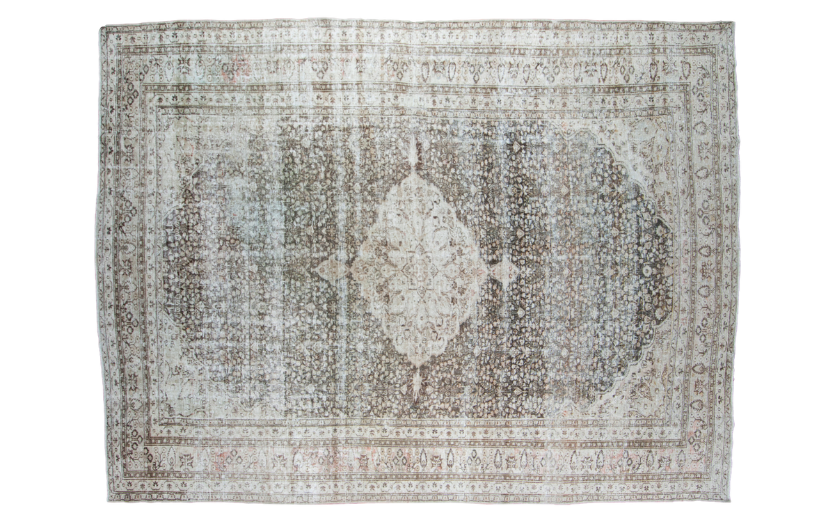 Distressed vintage Persian Meshed carpet, charcoal field, pale ivory medallion, blanched aesthetic.