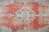 Textured distressed Oushak rug with soft red field and faded blue, ivory, pink central motif.