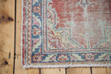 Distressed Oushak rug corner with soft red, sky blue, pink patterned border and fringe.