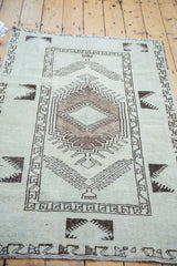 Distressed charcoal geometric pattern on soft ivory pile, vintage Oushak rug corner.