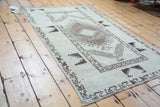 Corner detail of a distressed Oushak rug, displaying geometric charcoal patterns on pale ivory.