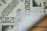 Distressed Oushak rug, folded corner revealing pale ivory pile and woven geometric backing.