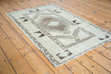 Distressed Oushak rug side, geometric border and faded charcoal patterns on pale ivory field.