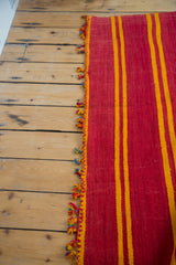 Woven edge detail of a vintage Moroccan Kilim rug with red, yellow, and blue tassels.