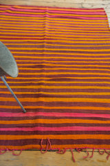 Eggplant, orange, and pink striped Moroccan kilim rug edge with woven wool fringe.