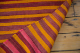 Moroccan kilim rug corner revealing eggplant purple, fire orange, and bright pink stripes.