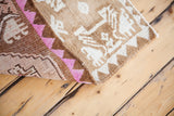 Folded Oushak rug corner revealing textured brown pile and bright rose geometric border.