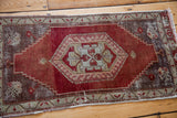 Distressed red field with faded grey spandrel motifs on vintage Anatolian rug corner.