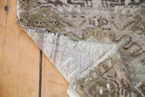 Curled Oushak rug corner showing geometric mauve, moss bronze pile and hand-knotted back.