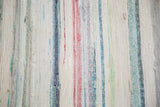 Hand woven rag rug texture with vertical stripes in pastel ivory, red, blue, and charcoal.
