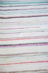 Hand-woven texture of vintage rag rug, featuring soft pastel and neutral stripes.