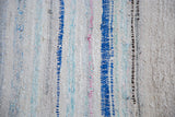 Textural detail of vintage hand woven rag rug with stripes in ivory, blue, pink, and gray.