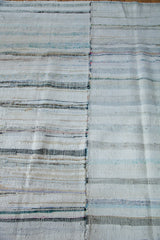 Hand woven rag rug seam with variegated stripes in pastel, ivory, and charcoal.