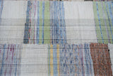 Hand-woven rag rug detail, displaying a plaid effect with pastel green, blue, ivory, and charcoal tones.