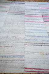 Hand-woven rag rug displaying variegated striped pattern with pastel, ivory, and ruby red tones.