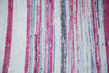 Hand-woven texture of vintage rag rug with ruby red, ivory, and varied pastel stripes.