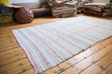 Textured edge of a vintage hand-woven rag rug with pastel and charcoal stripes.