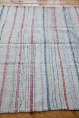 Frayed corner of hand-woven rag rug, showing textured stripes in pastel and neutral linen.
