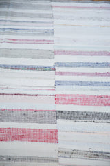 Hand-woven texture of the vintage rag rug, showing stripes of ivory, charcoal, and pastel hues.