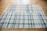 Angled close-up of the hand-woven rag rug's textured plaid in pastel and neutral stripes.