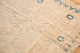 Khotan style carpet close-up, revealing worn ivory field, muted blue repeating motifs, and faded patterned border.