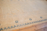 Detail view of the stylized blue border motifs and worn ivory Khotan carpet.