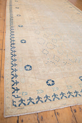 Faded blue medallion outlines and stylized border on the worn ivory Khotan carpet.